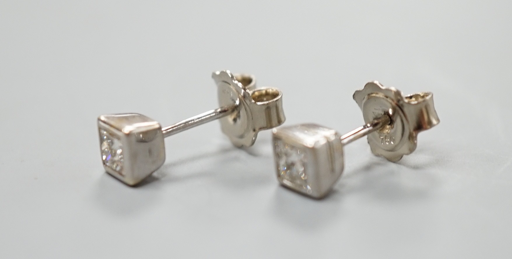 A pair of 750 white metal and princess cut solitaire diamond set ear studs, gross weight 2.4 grams.